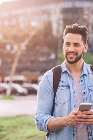 Young man on the street of big city , waiting taxi, chacking his smartphone, for news or new messages. Or looking for map instructions. Carry backpack on one shoulder. Casual dressed.